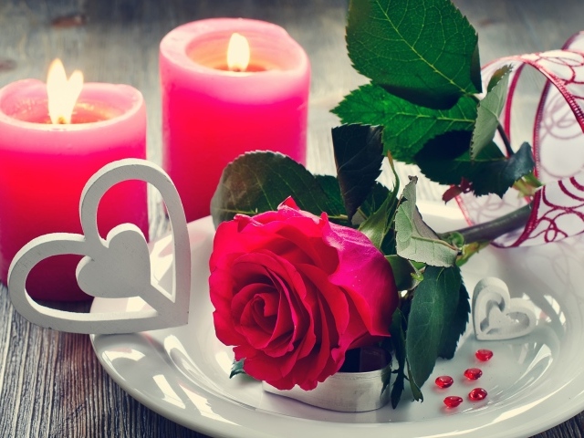 Красная роза на белой тарелке с сердечками на столе с зажженными свечами