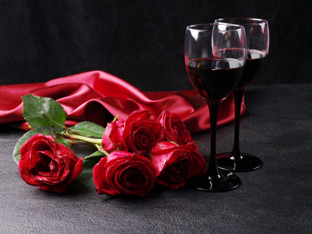 Два бокала с красным вином на черном фоне с букетом красных роз