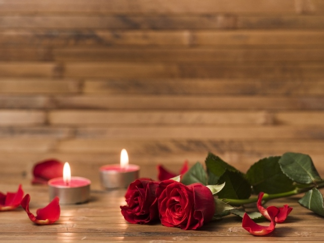 Две красные розы на столе с зажженными свечами 