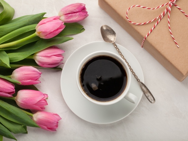 Белая чашка кофе на столе букетом розовых тюльпанов и подарком