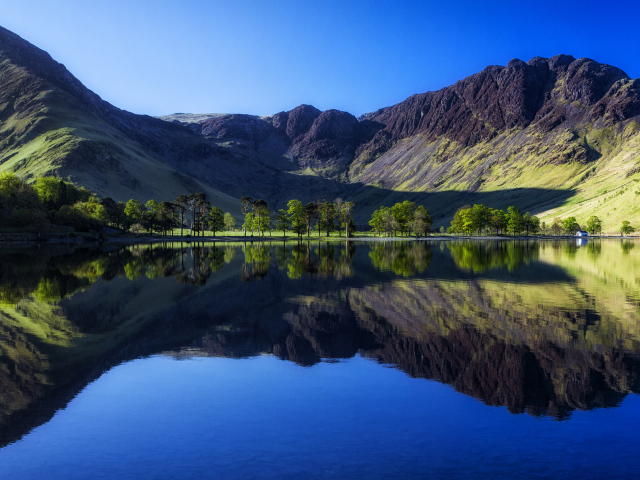 Черные высокие горы с голубым небом отражаются в воде озера
