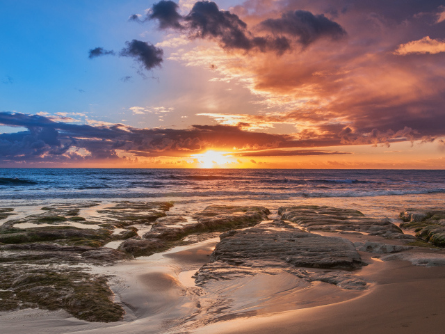 Мокрый песок и камни на берегу океана на закате солнца
