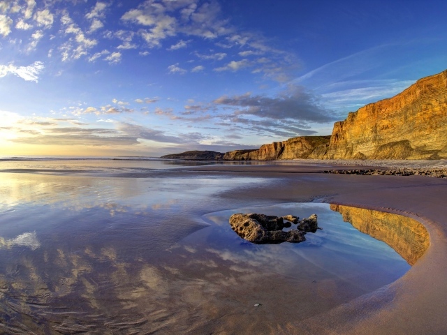 Мокрый морской берег со скалами на закате