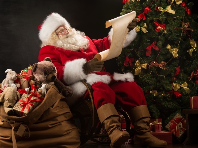 Санта Клаус с мешком подарков читает у елки