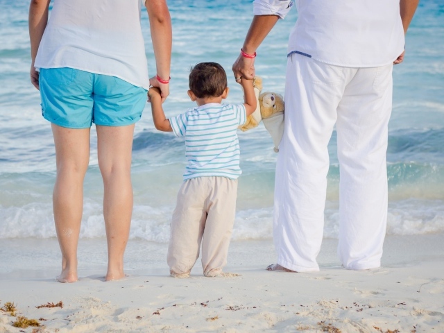 Семья с маленьким ребенком идет по пляжу