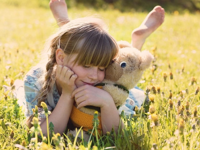 Девочка с игрушкой в руках лежит на траве 