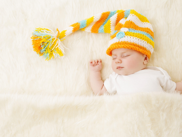 Маленький спящий под меховым покрывалом малыш в вязаной шапке