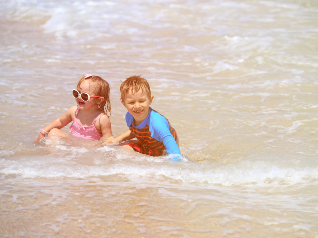 Маленькие мальчик и девочка купаются в море 