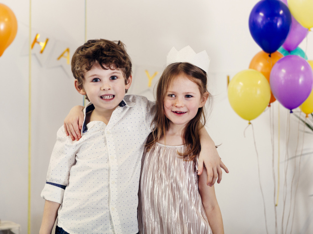 Маленькие мальчик и девочка на празднике с воздушными шарами