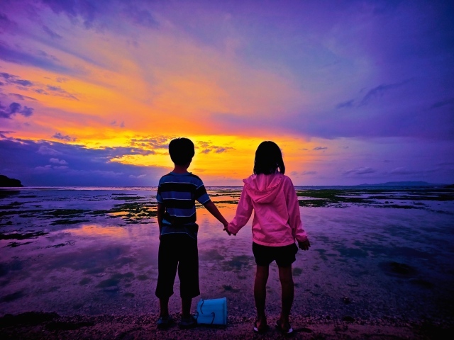 Маленькие мальчик и девочка стоят у воды на фоне заката 