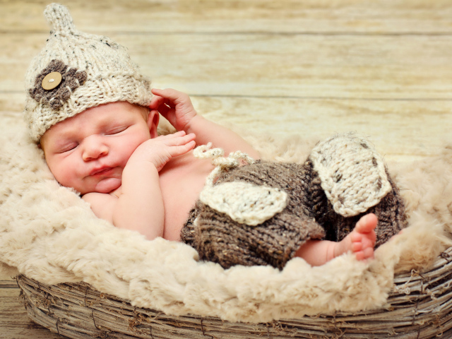 Маленький мальчик в вязаной шапке спит в корзине