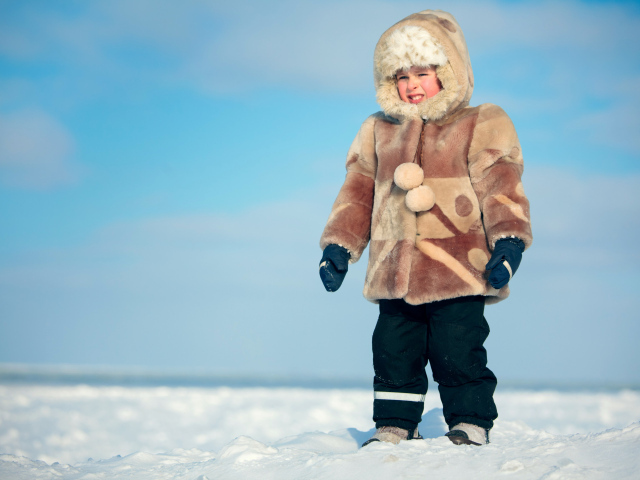 Маленький мальчик в теплой шубе на снегу 