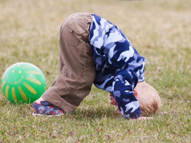 Маленький мальчик играет на траве с мячом
