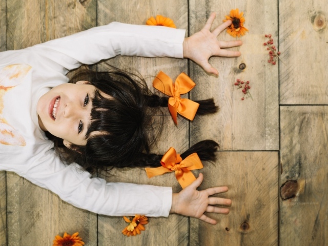 Маленькая веселая девочка с косичками лежит на полу