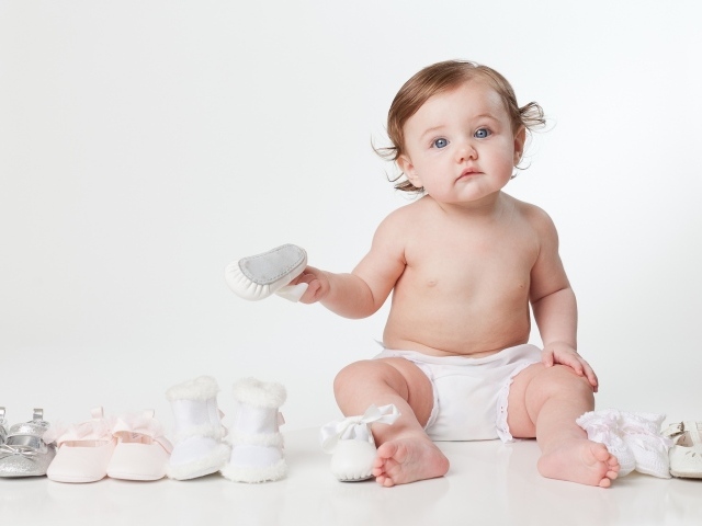 Маленький забавный голубоглазый малыш с обувью на белом фоне