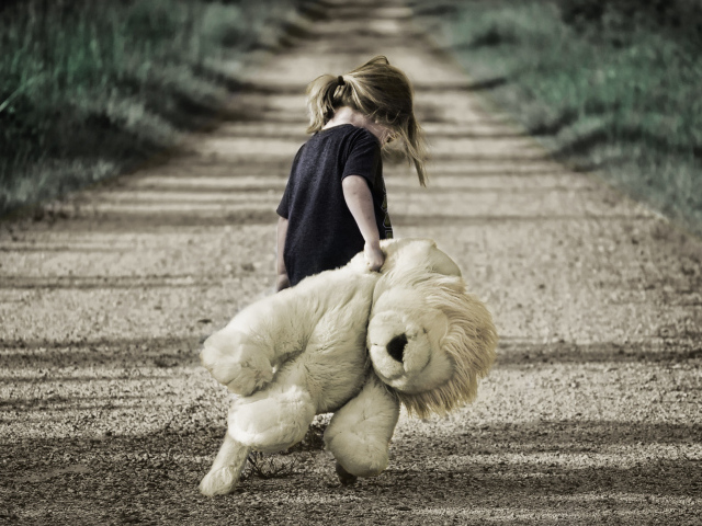 Маленькая девочка несет большую игрушку по дороге 