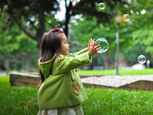 Маленькая девочка ловит мыльные пузыри на зеленой траве