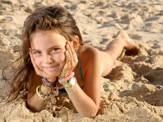Маленькая девочка лежит на песке на пляже