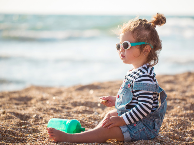 Маленькая девочка сидит на песке на пляже