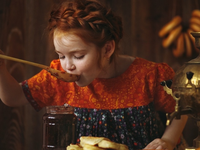 Маленькая рыжеволосая девочка пробует варенье