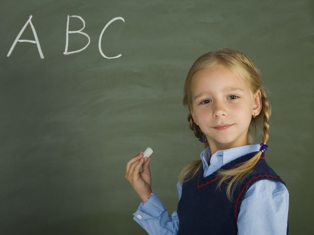 Маленькая школьница пишет буквы на доске 