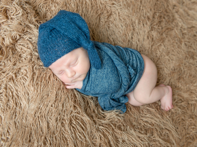 Маленький спящий грудной ребенок в синей вязаной шапке на меховом покрывале 