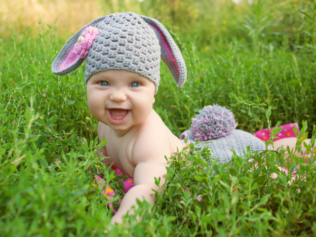 Маленький улыбающийся ребенок в костюме зайчика лежит в зеленой траве