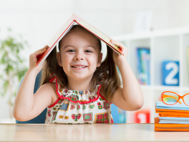 Маленькая улыбающаяся девочка с книгой на голове