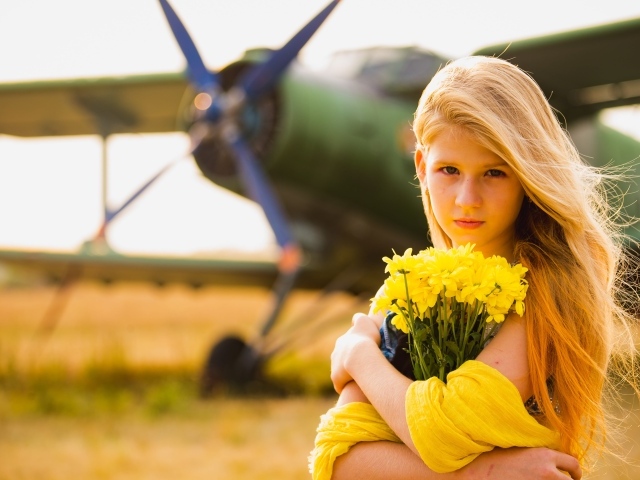 Длинноволосая девочка с букетом желтых хризантем на фоне самолета 