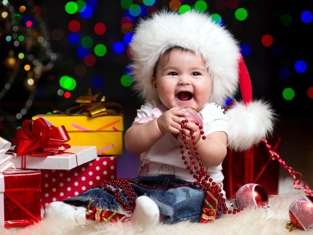 Улыбающийся малыш в новогодней шапке с подарками у елки