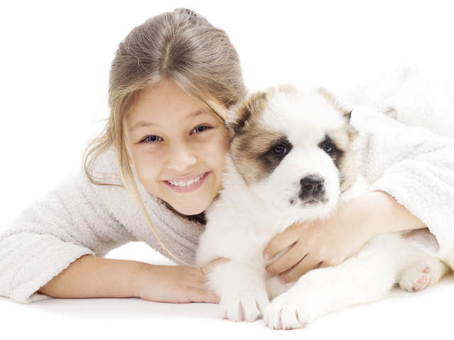 Улыбающаяся девочка лежит с щенком алабая