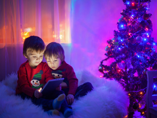 Два маленьких мальчика смотрят мультики у новогодней елки
