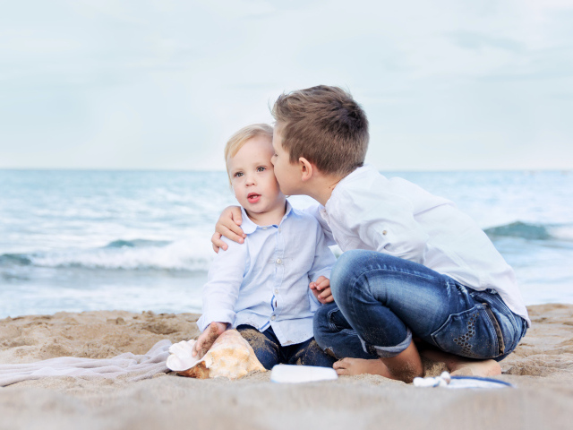 Два маленьких брата сидят на песке на пляже