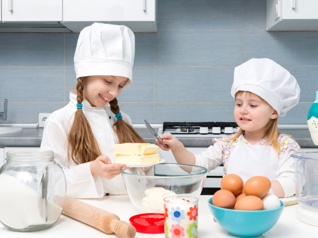 Две маленькие девочки в костюмах повара готовят на кухне