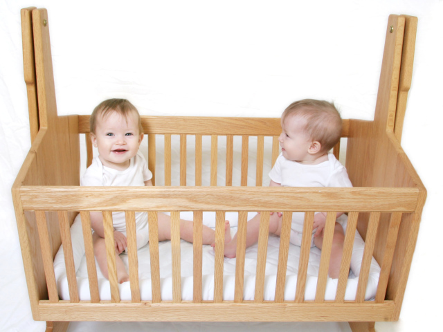 Два улыбающихся малыша в деревянной кроватке
