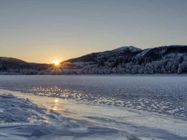 Покрытая льдом река у заснеженного леса на рассвете 