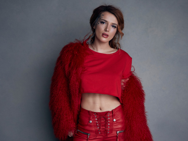 Актриса Белла Торн в красном наряде на фоне серой стены 