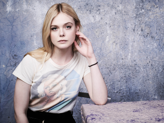 Актриса Эль Фаннинг сидит за столом у стены