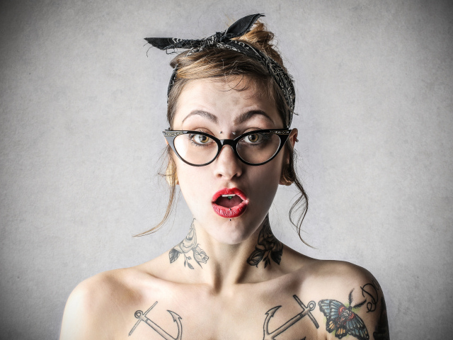 Удивленная девушка в очках с татуировками на теле