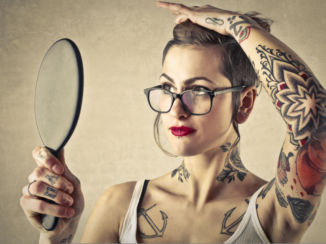 Девушка с татуировками на теле смотрит в зеркало