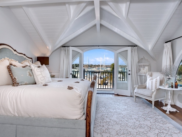 Белая спальня с большой высокой кроватью и балконом 