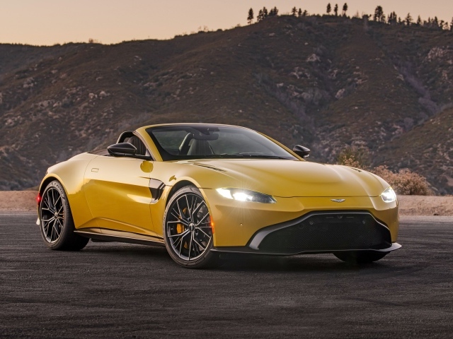 Желтый автомобиль  Aston Martin Vantage Roadster, 2021 года на фоне холмов