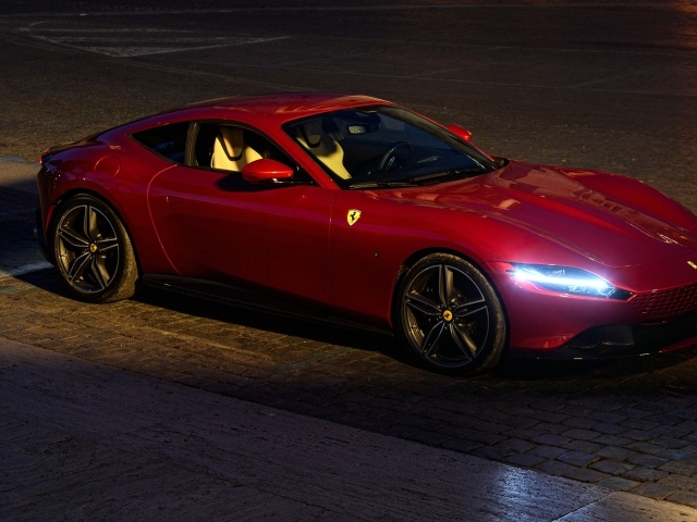Красный автомобиль Ferrari Roma 2020 года с включенными фарами вечером