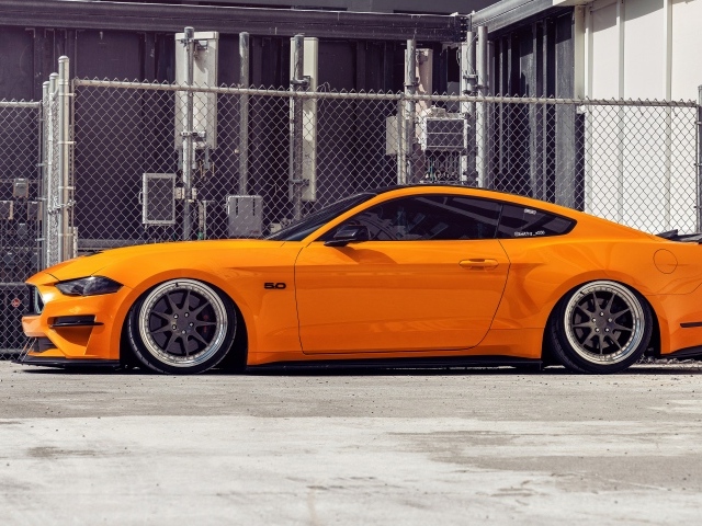 Оранжевый автомобиль  Mustang  у забора