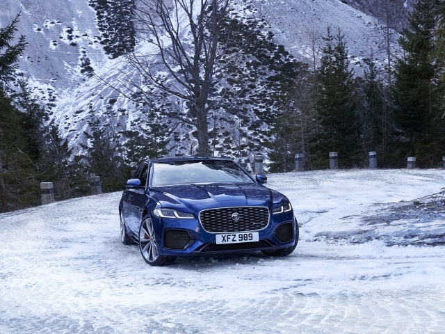Синий автомобиль Jaguar XF зимой на фоне горы 