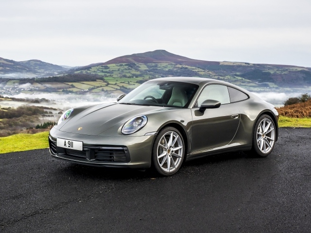 Серебристый автомобиль Porsche 911 Carrera на фоне холмов