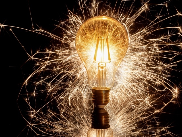 Зажженная лампа на черном фоне с искрами 