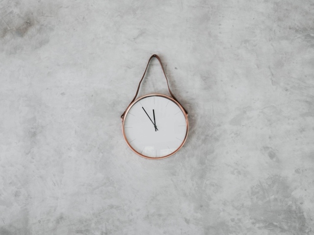 Часы с черными стрелками висят на серой стене 