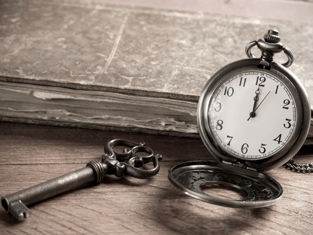 Карманные часы на столе с ключом и старой книгой 