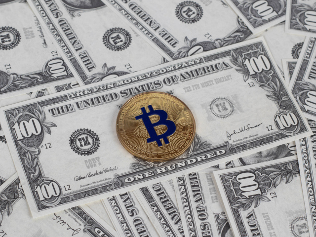 Монета Биткоин лежит на стодолларовых купюрах